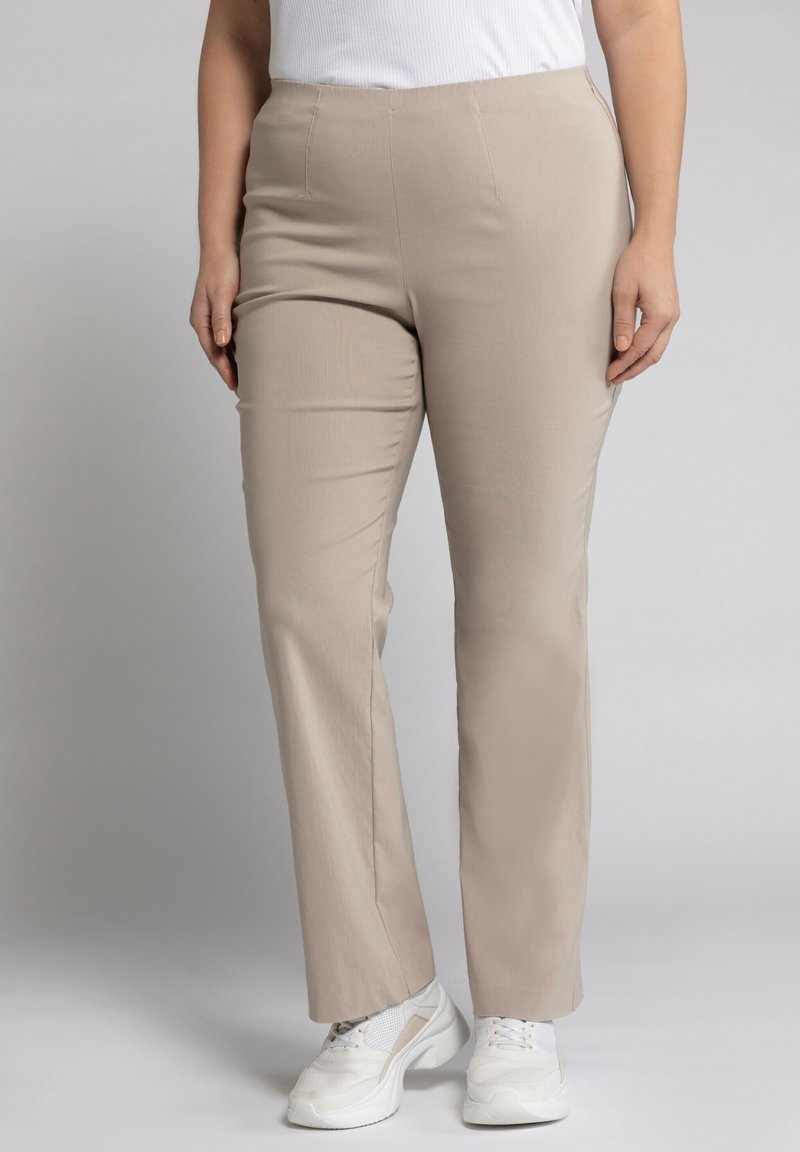 Pantalons beiges avec un design à jambe droite, en tissu lisse et avec une taille élastique, associés à des baskets blanches.