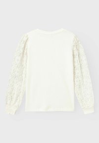 Camisa blanca de pulóver con cuerpo acanalado y mangas abullonadas de encaje transparente. Cuello redondeado y puños ajustados. Diseño minimalista con detalles elegantes.