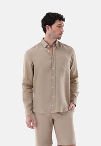 Langärmliges, hellbeiges Button-Up-Hemd aus atmungsaktivem Stoff; verfügt über eine Tasche, einen Button-Down-Kragen und eine subtile Textur.