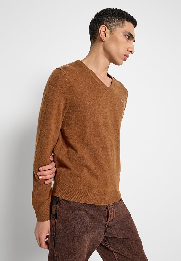 Brauner V-Ausschnitt-Pullover aus weichem Material, mit langen Ärmeln und taillierten Bündchen. Dezente Logodetails auf der Brust.