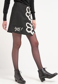 Mustahi mini skirt misi na uchapishaji wa maua meupe na neno "ndiyo!!" kwa maandiko ya mzunguko. Imeandaliwa na viatu vya ankle vya mblack na hoshi zisizo na uwazi. Muundo rahisi.