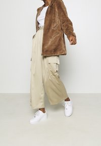 Brown faux fur jacket with a relaxed fit, paired with beige wide-leg satin pants and white sneakers, creating a comfortable look.