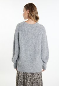 Hellgrauer, flauschiger Oversized-Pullover mit geripptem Muster, rundem Halsausschnitt und leicht ballonförmigen Ärmeln, getragen über einem Rock mit Blumenmuster.