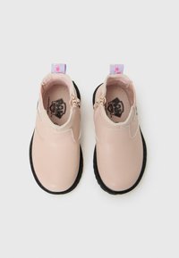 Bottines rose clair avec semelles noires, dotées de fermetures éclair et de tirettes à motif d'étoiles violettes, présentées sur un fond blanc.