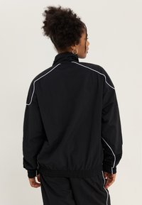 Must must jacket kõrge kraega, elastsete mansettide ja pasakaga. Omab valgeid triibu õmbluste ääres lisade detailina.