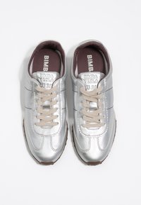 Srebrne metaliczne sneakersy o gładkim wykończeniu, okrągłym czubku, beżowych sznurowadłach i z logo na języku. Gumowa podeszwa z subtelnym wzorem przyczepności.