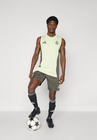 Zöld ujjatlan mez szürke oldalpanelek mellett, fekete rövidnadrág és fekete focizokni. Labda a lábaknál; Adidas márkajelzés látható a felszerelésen.