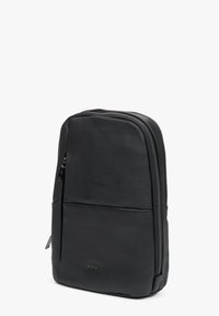 Černý kožený batoh s hladkou texturou, který má centrální zipové uzavření, přední kapsu a značkové logo na spodní straně.