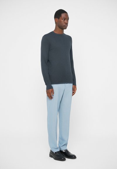 Dunkelgrauer, gerippter Langarmpullover kombiniert mit hellblauen, vertikal gestreiften Hosen und schwarzen Slippers. Schlichte Gestaltung und Passform.