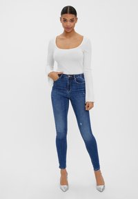 Vit ribbad långärmad topp med fyrkantig halsringning och utsvängda ärmar, som är ihopparad med högmidjade blå skinny jeans och silverklackar.