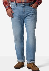 Jeans de mezclilla azul claro con un diseño de pierna recta, que cuentan con un cierre de botón y cremallera, cinco bolsillos y los dobladillos enrollados. Llevados con botas marrones.