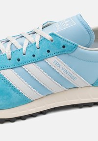 Ljusblå sneakers med vitt tre-stripesdesign, i mocka och syntetiska material, med texturerade sulor och logodetalj på tungan.