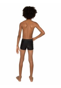 Shorts de bain noirs au design uni, avec une ceinture texturée portant l'étiquette "PROTEST". Le tissu est lisse avec une coupe ajustée.