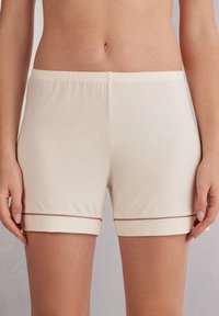 Světlé béžové bavlněné šortky s uvolněným střihem, které mají měkký elastický pas a kontrastní tmavý lem na spodním okraji.