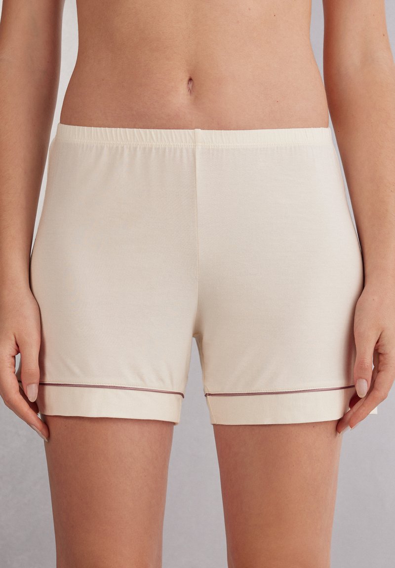 Světlé béžové bavlněné šortky s uvolněným střihem, které mají měkký elastický pas a kontrastní tmavý lem na spodním okraji.