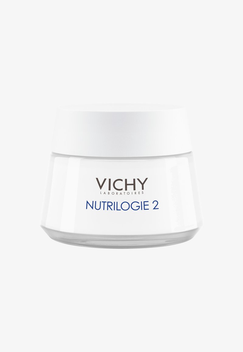 Weißes Glasgefäß mit breiter Basis und schmalem, abgerundetem Deckel. Auf dem Etikett sind "VICHY" und "NUTRILOGIE 2" in grauem und blauem Text zu sehen. Glatte Oberfläche.