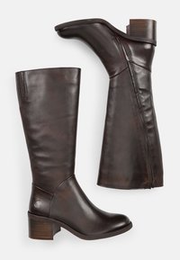 Bottes en cuir marron, hautes jusqu'au genou, avec un bout arrondi, un talon bloc et une fermeture éclair sur le côté. Elles présentent des nervures horizontales sur la tige supérieure.