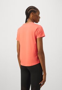 Camiseta atlética de manga corta color coral con textura suave, cuello redondeado y corte relajado, combinada con leggins negros.