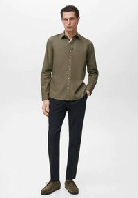 Olivgrünes Langarmhemd mit Knopfverschluss, kombiniert mit schwarzen Hosen und braunen Schuhen. Einfaches Design und glatte Textur.