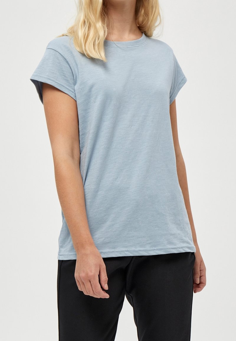 Světle modré tričko s krátkými rukávy vyrobené z jemné tkaniny, s kulatým výstřihem a ohrnutými rukávy. Pohodlný střih, jednoduchý design.