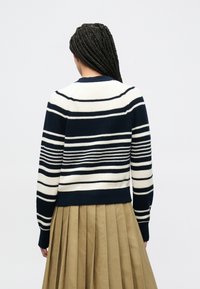 Πλεκτό πουλόβερ με ρίγες σε ναυτικό μπλε και κρεμ χρώμα, με ριμπ τελείωμα στο κάτω μέρος και στα μανίκια. Η πίσω όψη δείχνει λεπτομέρεια στη ραφή των ώμων και υφασμένες ρίγες.