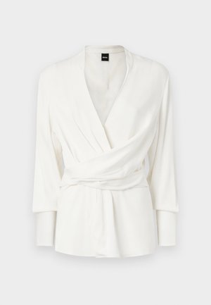 Bijela bluzica s dugim rukavima, V-izrezom i detaljem remena u struku. Izrađena od glatkog, padajućeg materijala.