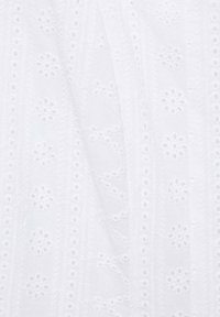 Vit tyg med broderade blommönster och hålstickade detaljer, med en mjuk, texturerad yta och genomskinlig känsla.