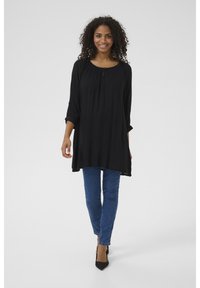 Tunique noire avec un col rond et des détails de boutons, associée à un jean skinny bleu et des escarpins noirs à talons pointus. Tissu lisse, coupe décontractée.