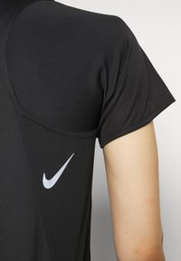 Camiseta atlética negra de manga corta, con una tela texturizada y un logotipo blanco de Nike situado en la costura del hombro izquierdo.