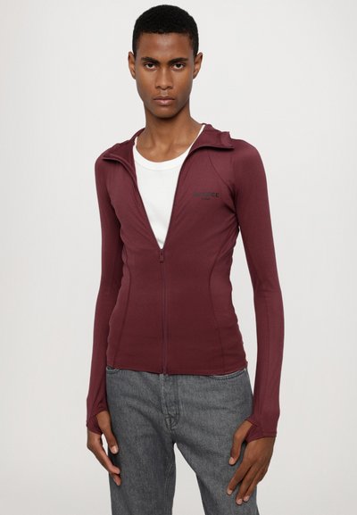 Bordo zip-up jakna s dugim rukavima, uskog kroja, meke teksture, s malim crnim logotipom i otvorima za palceve na manžetama.