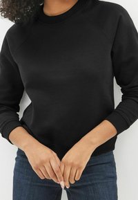 Schwarzer Pullover mit Rundhalsausschnitt, gerippten Bündchen und Saum. Weicher Stoff mit glatter Textur. Trägt er mit dunkelblauen Jeans.