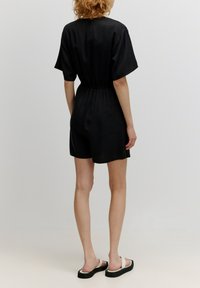 Zwarte jumpsuit met korte mouwen en een elastische taille, met een gladde textuur en een losse pasvorm, die eindigt boven de knieën.