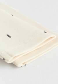 Kerman värin kangas, joka on taitettu ja jossa on mustia täpliä. Materiaali näyttää pehmeältä ja reunassa on näkyvissä ompeleet.