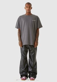 Grå oversized bomull T-skjorte med hvit tekst. Svarte blanke vide bukser og rosa joggesko med hvite snører. Tatoveringer synlige på armene.