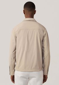 Beige jas met lange mouwen, een kentkraag en zijsplitten; gladde stof met een eenvoudig ontwerp, dat een schone, minimalistische esthetiek toont.