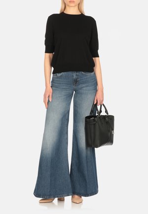 Top in maglia nera a maniche corte, jeans svasati azzurri chiari con sfumature graduali, tacchi nude, mentre tiene una borsa nera testurizzata.