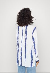 Camicia a maniche lunghe con un motivo tie-dye blu e bianco, realizzata in tessuto leggero, con dettaglio a bottoni sul retro e fessure laterali.
