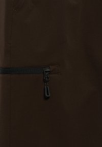 Close-up of dark brown fabric with black horizontal zipper and pull tab.