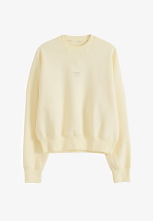 Vaaleankeltainen pyöreäkauluksinen collegepaita, jossa on pitkät hihat ja pieni, keskitetty kirjailtu logo rinnassa.