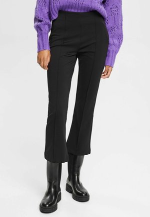 Person wearing black fitted cropped pants, black chunky boots, and a purple long-sleeve knit sweater with textured pattern.