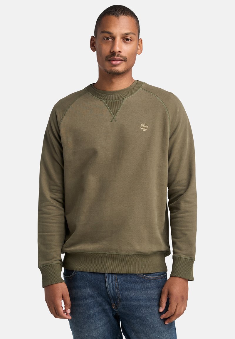 Sudadera verde oliva con cuello redondo ribeteado y puños, featuring a logo en el pecho. La tela parece suave y con textura. Se lleva con jeans.