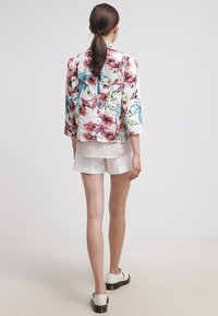 Kurtka w kwiatowy wzór z lekkiego materiału, z rękawami do połowy przedramienia i dopasowanym krojem. Dopełnieniem stroju są białe szorty.