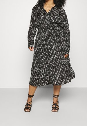 Schwarzes langärmliges Kleid mit einem weißen Diamantmuster, tailliert mit einem passenden Gürtel. Kombiniert mit schwarzen Sandalen mit Riemchen.