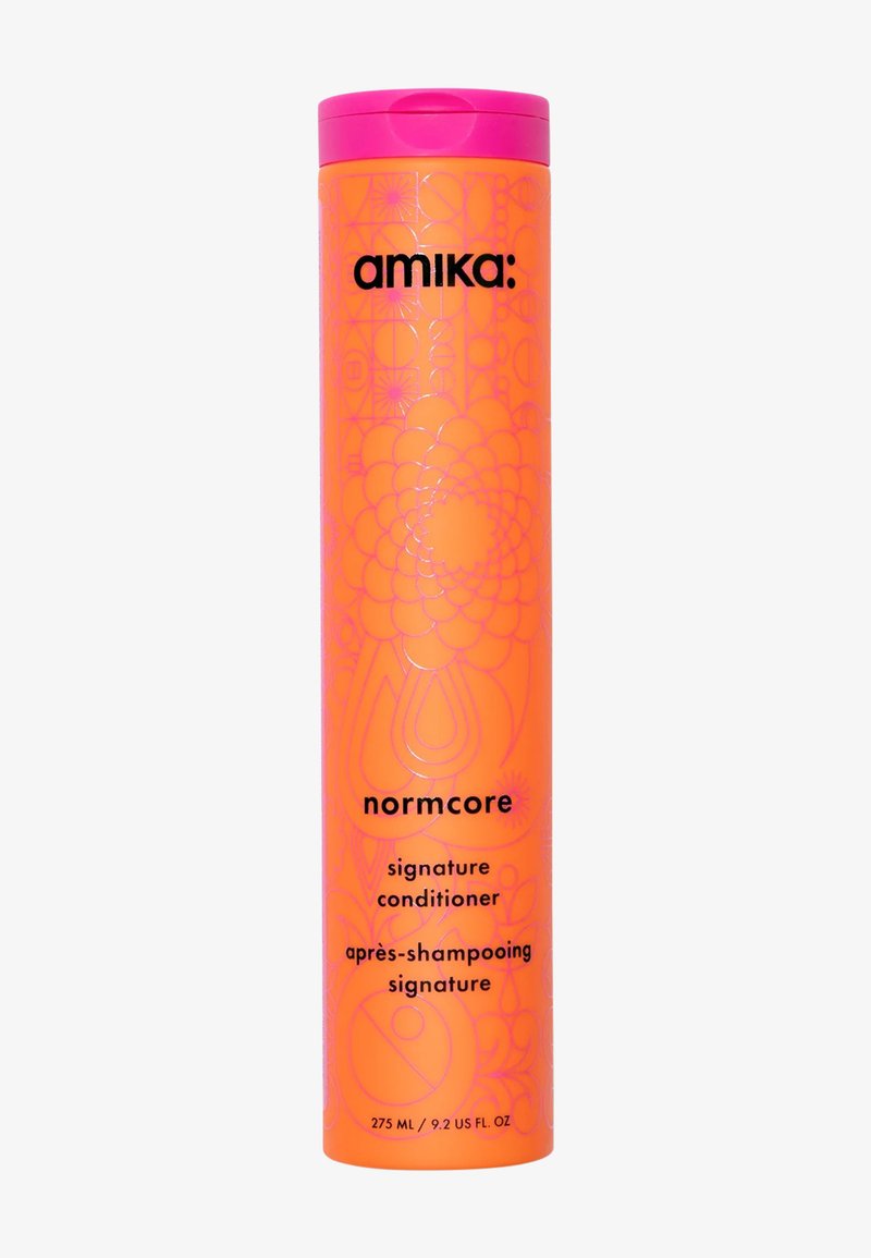 Bouteille cylindrique orange avec un couvercle à clapet rose, motifs géométriques en relief, et texte noir indiquant "amika : après-shampoing signature normcore".