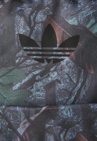 Multikleurige stof met een donker bloemmotief en een centraal zwart Adidas-logo met drie strepen eronder. Duurzaam, gestructureerd oppervlak.