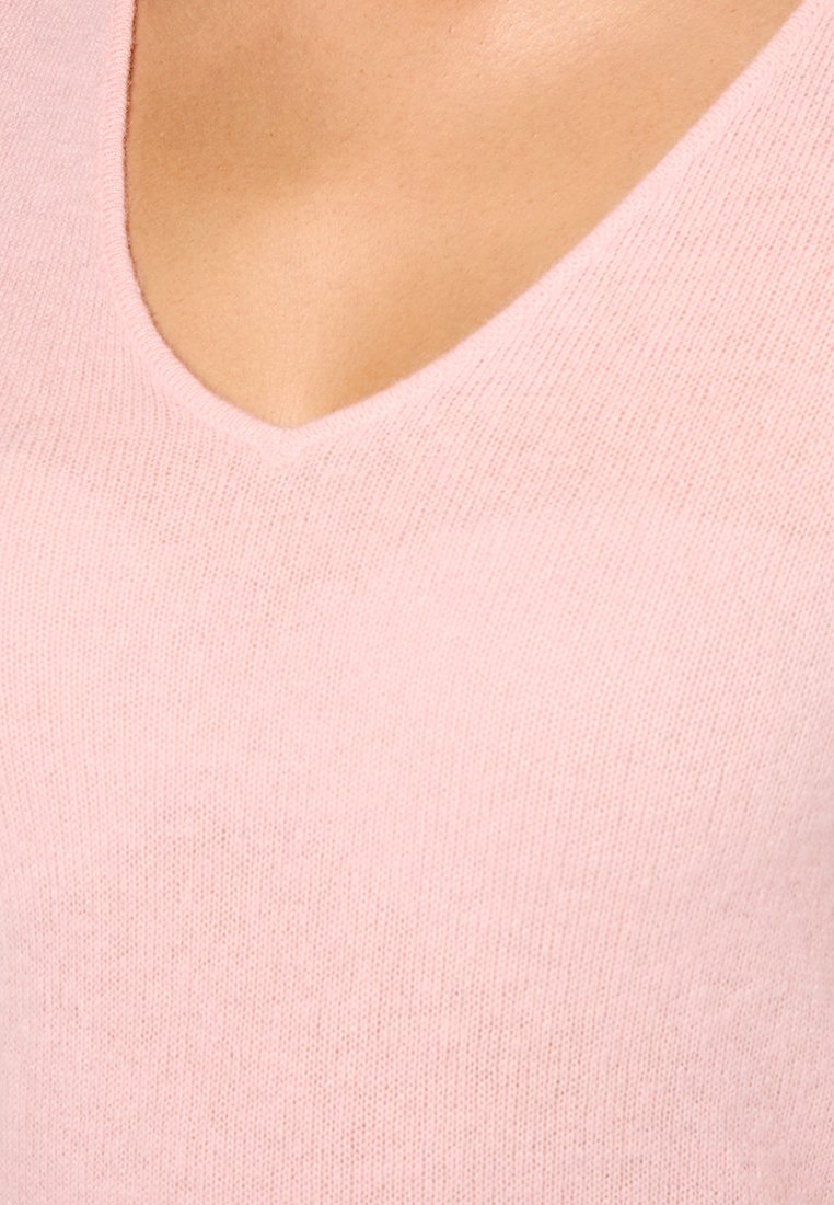 Jasnoróżowy sweter wykonany na drutach z dekoltem w kształcie V i miękką fakturą, podkreślający cienkie włókno i bezszwowy design.