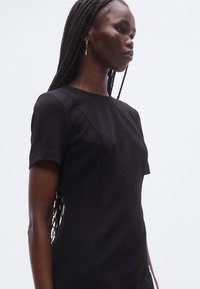 Vestido preto de manga curta com design elegante, feito de tecido suave. Apresenta decote redondo e silhueta ajustada.