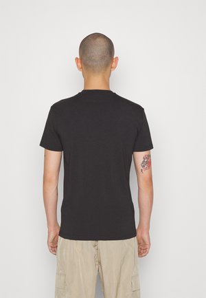 Musta puuvillainen T-paita, jossa on pyöreä pääntie, lyhyet hihat ja rento istuvuus, yhdistetty vaalean beigeihin cargo-shortseihin.