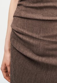 Κοντινό πλάνο ενός ατόμου που φοράει καφέ ριγωτή υφασμάτινη φούστα και τοπ, εμφανίζοντας τη λεπτομέρεια του υφάσματος και μέρος του αριστερού του χεριού.