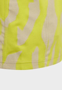 Ljusgul tyg med ett beige abstrakt mönster, slät textur och synlig sömnad längs fållen.